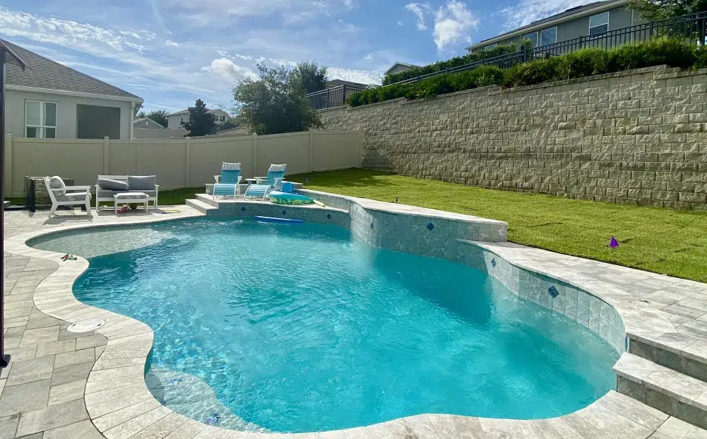 Freeform in-ground pool shape with curved edges and stone paver deck in a residential backyard