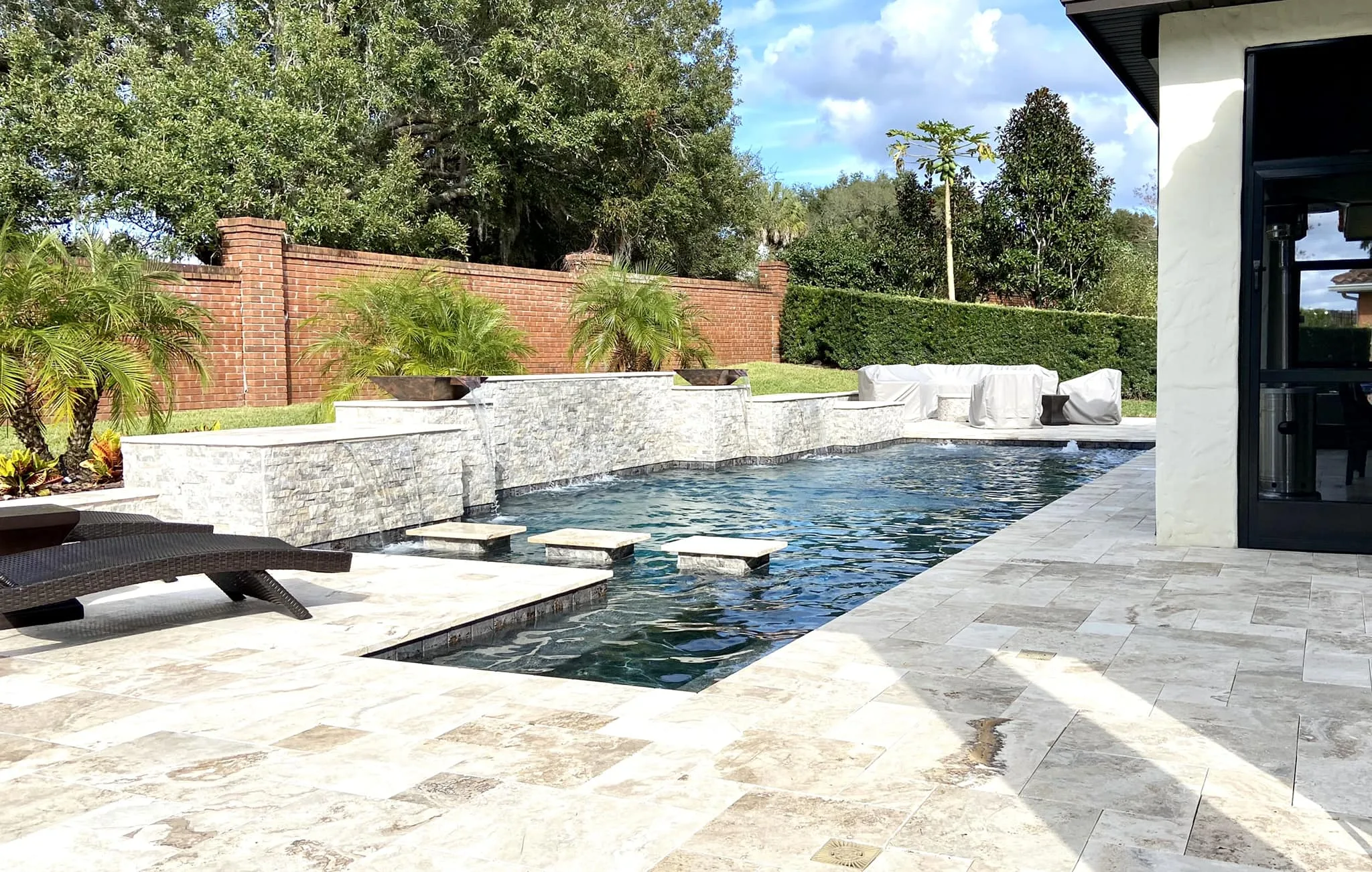 Modern in-ground concrete pool with raised water feature and stone patio in a spacious Orlando backyard.
