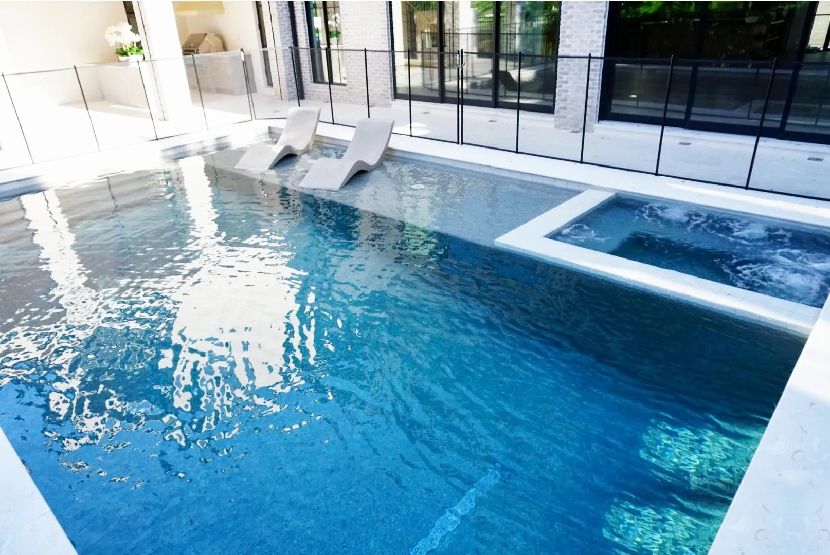 Modern backyard pool with integrated spa, tanning ledge loungers, and surrounding outdoor living space design