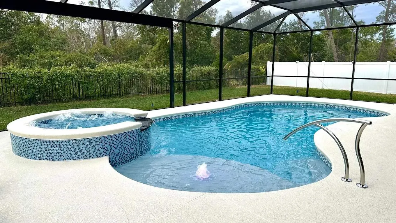 Freeform screened pool with a raised circular spillover spa, tanning ledge bubbler, and white pool deck