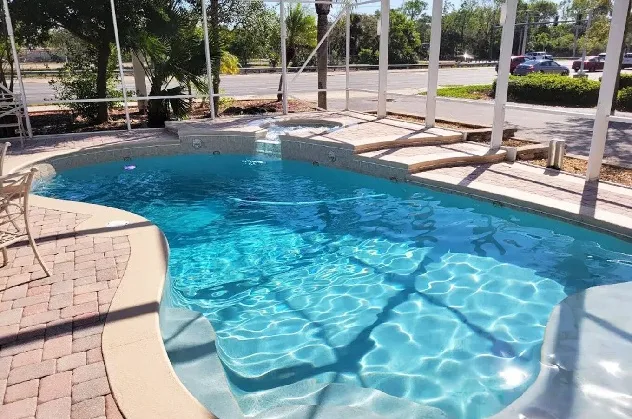 Freeform screened swimming pool with curved entry steps, an attached round spa, and a brick paver deck