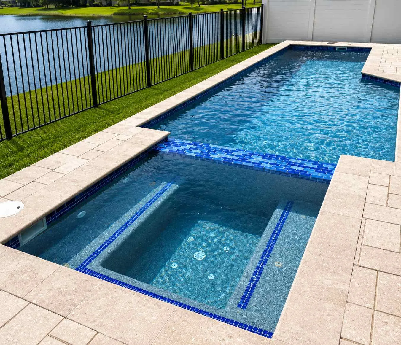 Geometric lakefront pool with an attached square spa, built-in bench seating, blue tile accents, and a light paver deck in Daytona Beach