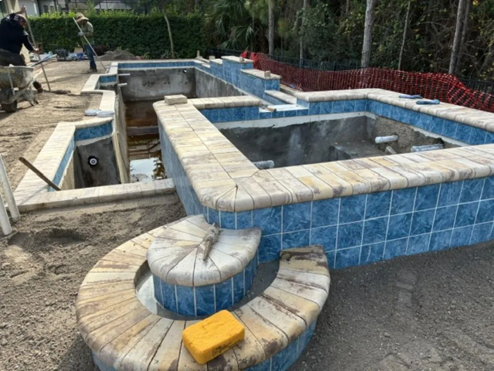Pool and attached spa remodel in progress by Artesian Pools in Daytona Beach, showing new blue tile, coping, and resurfacing preparation