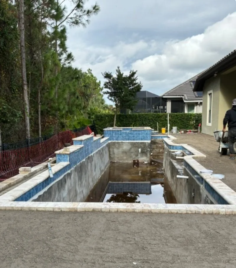 Drained swimming pool undergoing resurfacing preparation by Artesian Pools in Daytona Beach, with exposed interior walls, blue waterline tile, and coping