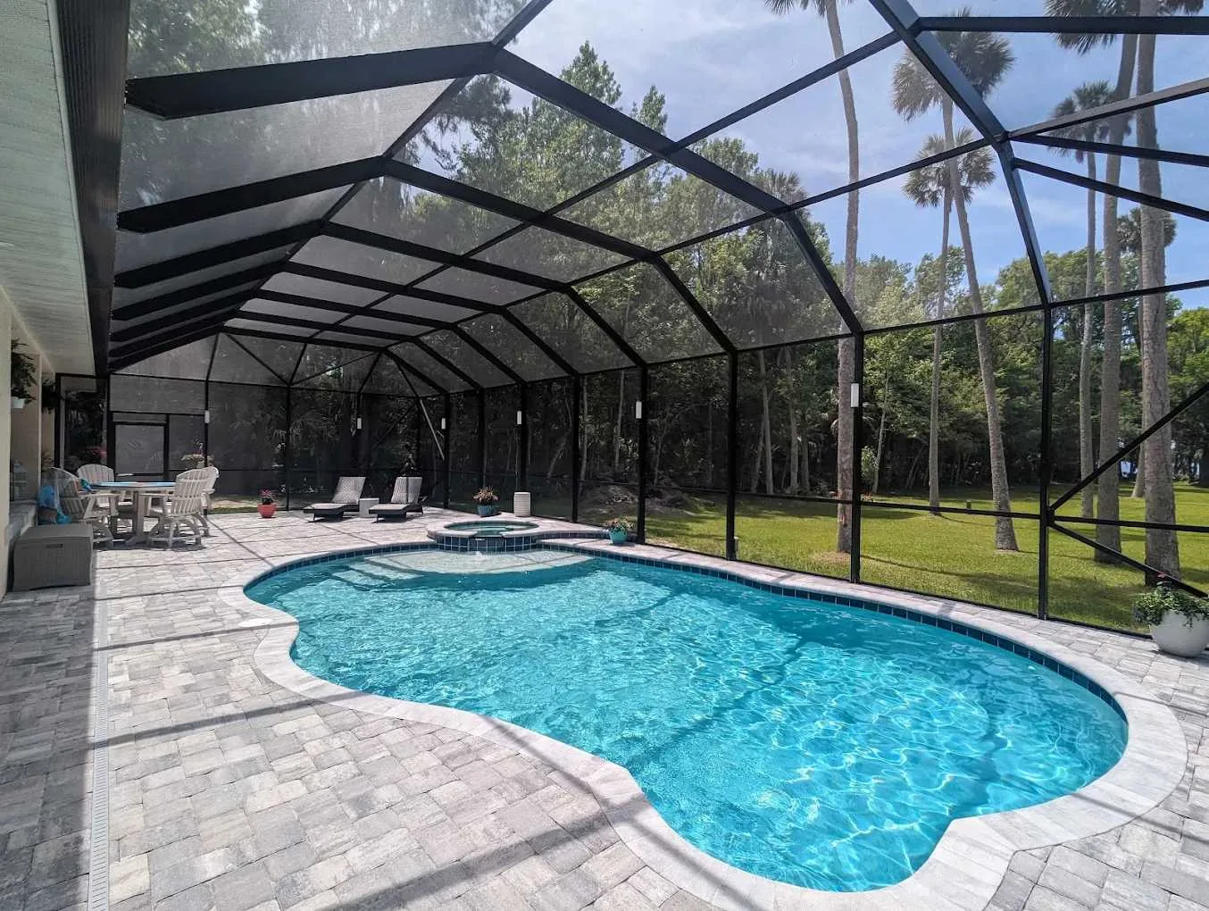 Screened freeform pool with an attached raised spa, paver deck, and spacious covered outdoor living area in Daytona Beach