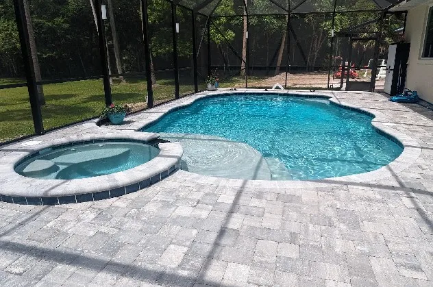 Screened freeform pool with an attached round spa, shallow sun shelf, curved entry steps, and gray paver deck in Daytona Beach
