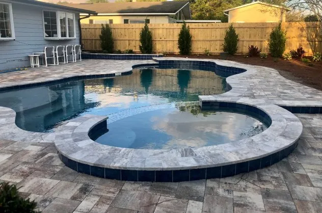 Freeform custom pool with an attached raised round spa, blue waterline tile, and stone paver deck in an Orlando backyard